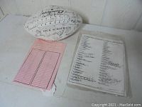 White autographed football with visible black signatures, some faded from sun exposure. Ball branded Baden with laces intact. Accompanied by a pink receipt and a signed list of participants.