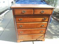 Front view of cherry wood tall boy dresser showing six drawers and spindle side columns with brass handles.