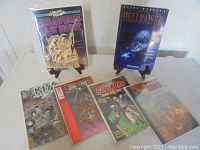 Full set of six comic books displayed, two standing on small easels and four laid flat, showing varying cover art styles and themes.