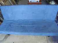 Dark blue futon in upright sofa position, showing tufted fabric upholstery and metal legs on concrete floor.