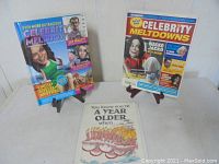 Lot of two pop-up celebrity story books and a humorous birthday card, displayed on small stands and lying flat.