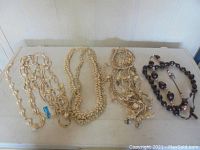 Photo showing four distinct handmade shell necklaces laid flat on a surface, including cream-colored shell strands and one with larger dark beads.