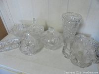 Seven clear cut and crystal glass pieces arranged including covered dishes, crystal dish, and tall vase.