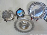 Four metal platters and plates shown on stands and flat, including a colorful butterfly wing plate and a Mikasa platter.