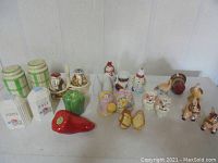 Full set of 24 assorted salt and pepper shakers displayed on white surface, showing variety of shapes and colors including chili pepper, green pepper, owls, and baskets.