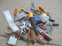 Overhead photo showing the assortment of estate tools arranged on a flat surface including screwdrivers, clamps, measuring tapes, and a caulking gun.
