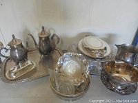 Full view of various silver plate pieces including pots, trays, bowls, and glass dish