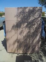 Full view of the three-panel folding room divider outdoors showing the light pink woven texture and overall structure.