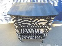 Front view of the small black and white zebra hand-painted nightstand showing the zebra striped drawers, metal studs, and black top surface.