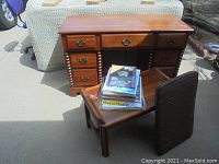Oak desk with several drawers, metal handles, and wooden legs. Desk top has some scratches visible. A small wooden chair with a fabric upholstered back and seat is resting against the desk.