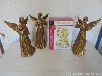 Photo showing three gold-tone angel figurines and a boxed brass-colored musical Ferris wheel, confirming count and style