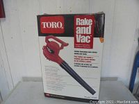 Photo of the Toro Rake and Vac product box showing the red handheld leaf blower and vacuum unit with black nozzle, product details and model number 51549.