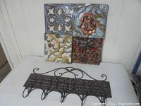 Photo of heavy metal coat rack with five hooks and an ornamental scrollwork top mounted against a wall.