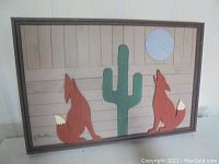 Framed original lath art facing forward, showing desert landscape with two foxes, a cactus, and sun/moon.