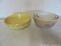 Photo of four bowls: one yellow Hall bowl and three nested beige Pyrex bowls with floral pattern.