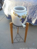 Front view of the ceramic water cooler on wooden stand, showing grapevine decoration and water spout