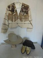 Western-themed jacket hanging on wall above cowboy hat and boots on table.