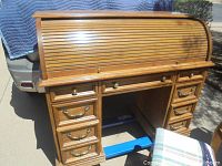 Front view of wooden roll top desk with closed tambour top and visible lower drawers with brass handles.