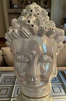 Front close-up showing textured hair with holes, smooth facial features, and iridescent finish.