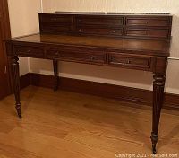 Front angled view of dark wood desk showing three front drawers and fluted legs with brass casters