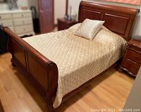 Full view of dark wood queen sleigh bed with mattress and bedding on hardwood floor