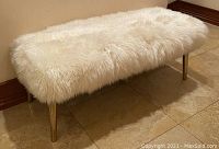 Front right angled view of white sheepskin upholstered bench on tile floor