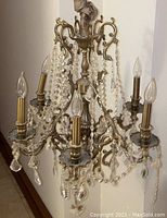 Full view of the bronze chandelier showing six ornate arms with candle-style fixtures and hanging crystal beads and pendants.