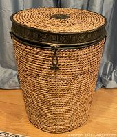 Front view of large woven hamper basket showing metal trimmed lid and latch closure
