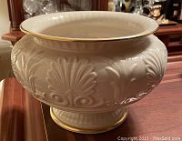 Ivory/cream wide Lenox vase with embossed decorative motifs and gold rim taken from a front angle showing detail.