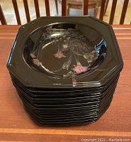 Stacked large black octagonal plates with pink and gray floral accents on glossy finish surface.