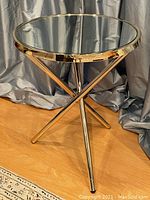Side view of the round side table showing the mirrored glass top and gold-tone metal tripod legs.