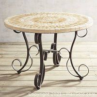 Photo shows round coffee table with beige and cream mosaic tile top and black wrought iron scrollwork base on a wooden floor background.