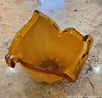 Top view highlighting the ruffled edge and orange color of the Murano glass vase on a stone countertop.
