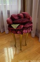 Side angle of custom red velvet flower petal stool showing gold wooden legs on hardwood floor