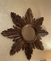 Starburst mirror showing the antique brass color painted wood-like frame and round reflective mirror center mounted on a textured wall.