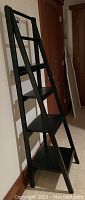 Angled side view of black ladder-style bookshelf showing tiered shelves
