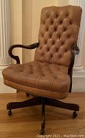 Three-quarter front view showing tufted leather seat, armrest and wood base with casters