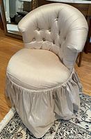 Front angle view showing tufted button backrest, cushioned rounded seat, gathered skirt reaching floor.