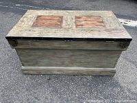 Front angled view of the wooden storage chest showing the distressed finish and black hardware along the lid edges.