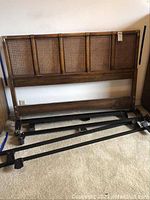 Full view of the wooden bed frame headboard with cane panel inserts and metal support rails laid out on the floor.