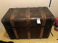 Front view of a large vintage wooden trunk with dark worn wood and metal decorative corners and vertical strap reinforcements.