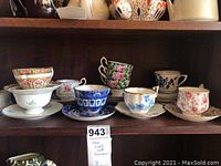 Multiple floral and patterned fine china teacups and saucers arranged on a shelf.