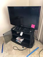 Full setup with LG 32-inch television placed on a black TV stand which has a glass door and space holding DVDs and electronics. Power cables and remote controls visible.