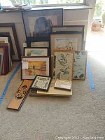 Multiple framed and unframed prints leaning against wall including images of nature scenes such as lakes, birds, ocean, and architectural prints.