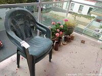 View of a green plastic outdoor chair on a balcony with flower pots and plant dirt spread on the floor surface.
