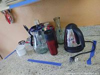 Side view of vintage electric coffee pot, travel mugs, glass pitcher, coffee filter, and ramekin bowls on countertop.