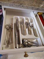 View of flatware and flatware tray inside a kitchen drawer showing knives, forks, spoons, and teaspoons.
