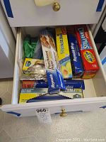 Drawer full of various kitchen wraps including Reynolds Parchment Paper, Glad Press'n Seal, Cling Plus plastic wrap and aluminum foil, along with some storage bags.