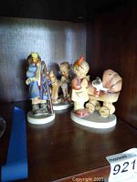 Photo of three Western Germany Hummel figurines depicting children in various scenes, on display shelf