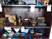Photo of shelf with various brass items, bookends, porcelain cups and bowls